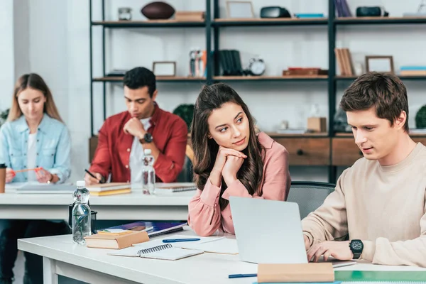 Multiethnische Studenten, die am Schreibtisch sitzen und Laptop benutzen, während sie im Klassenzimmer lernen — Stockfoto