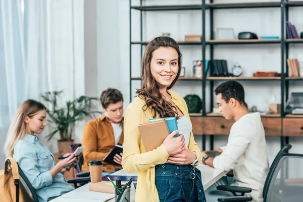 Charmant lächelnder Student steht am Tisch und hält Bücher — Stockfoto