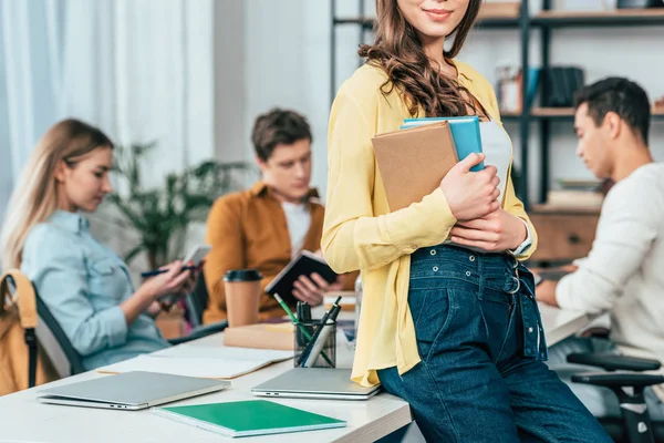 Ausgeschnittene Ansicht einer brünetten Studentin, die am Tisch steht und Bücher hält — Stockfoto