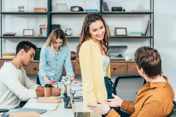 Quattro studenti multiculturali sorridenti con computer portatili e libri che studiano insieme — Foto stock