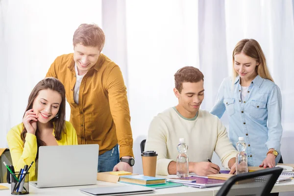 Quatro estudantes sorrindo multiétnicos com laptops e livros estudando juntos — Fotografia de Stock