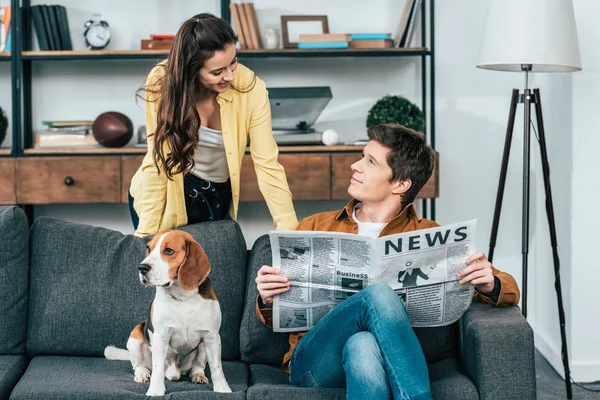 Чоловік з собакою читає газету на дивані і дивиться на дівчину — стокове фото