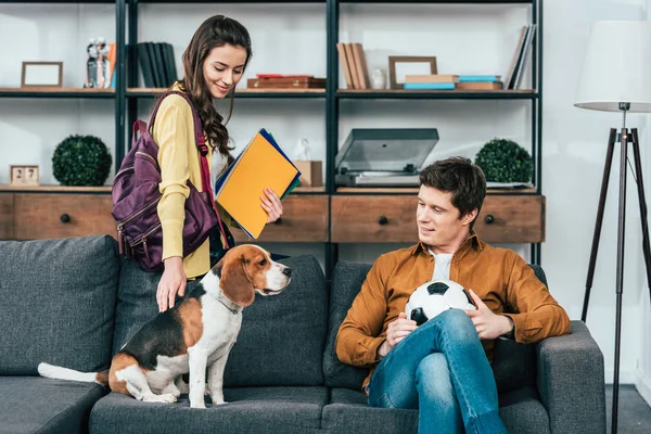 Studentin mit Rucksack und Notizbuch streichelt Beagle-Hund auf Sofa — Stockfoto