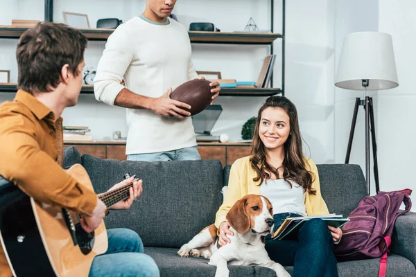 Tres amigos con perro beagle tocando la guitarra en la sala de estar - foto de stock