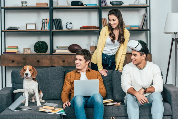 Tres amigos multiculturales riendo con perro usando auriculares vr en la sala de estar - foto de stock