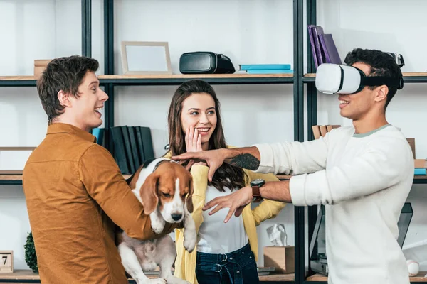 Three laughing friends with dog using vr headset in living room — Stock Photo