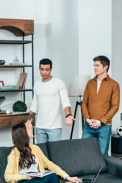 Trois étudiants multiethniques avec ordinateur portable et réserver dans un salon confortable — Photo de stock