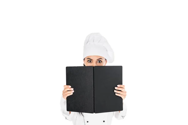 Schockierter Koch in Uniform hält schwarzes Buch auf weißem Hintergrund — Stockfoto