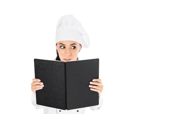 Curious chef in uniform holding black book isolated on white — Stock Photo