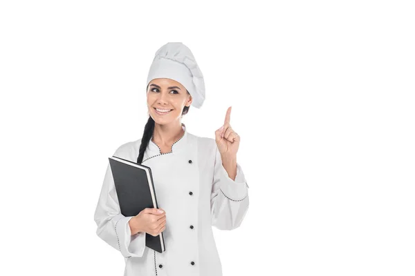 Chef em uniforme segurando livro preto e mostrando gesto ideia isolado no branco — Fotografia de Stock