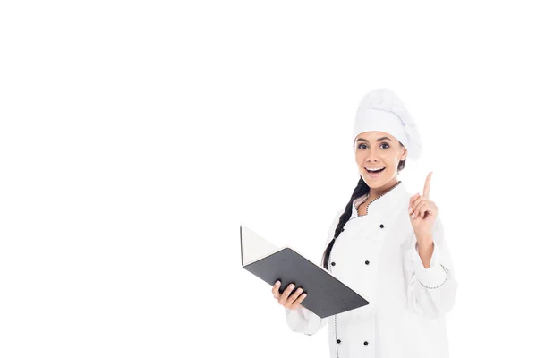 Chef incrível em uniforme segurando livro preto e mostrando gesto ideia isolado no branco — Fotografia de Stock