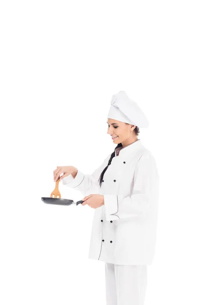 Chef in hat holding frying pan and wooden kitchen spatula isolated on white — Stock Photo