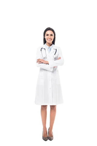 Vue pleine longueur du médecin joyeux en manteau blanc debout avec les bras croisés isolés sur blanc — Photo de stock