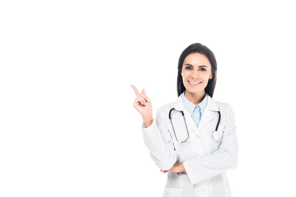 Lächelnder Arzt im weißen Mantel mit Stethoskop, das mit dem Finger auf Weiß zeigt — Stockfoto