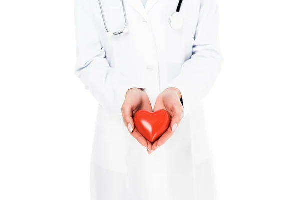 Обрезанный вид врача в белом халате с пластиковым сердцем, изолированным на белом — стоковое фото