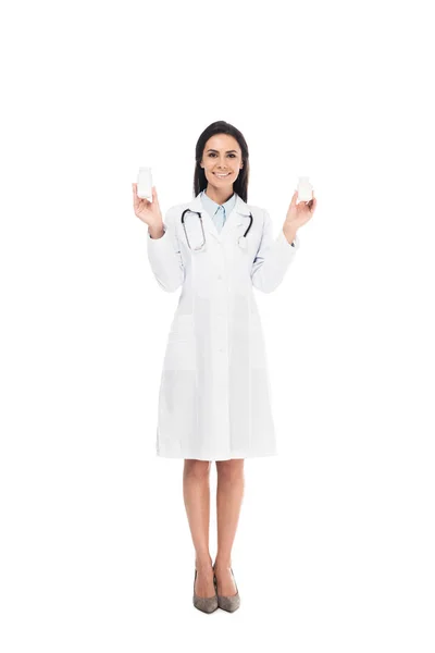 Ganzkörperansicht des Arztes im weißen Kittel mit Stethoskop, das Tabletten isoliert auf weißem Untergrund hält — Stockfoto
