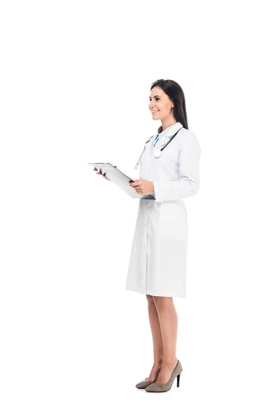 Volle Länge des lächelnden Arztes in weißem Mantel mit Klemmbrett isoliert auf weiß — Stockfoto