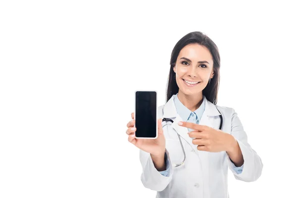 Arzt in weißem Mantel mit Stethoskop zeigt mit dem Finger auf Smartphone mit leerem Bildschirm isoliert auf weiß — Stockfoto