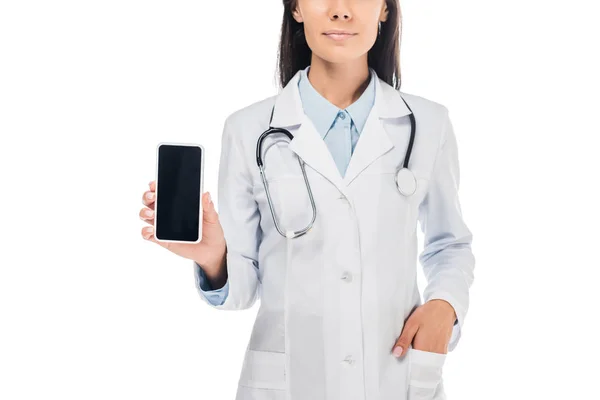 Vista recortada del médico en bata blanca con estetoscopio que sostiene el teléfono inteligente con pantalla en blanco aislado en blanco - foto de stock