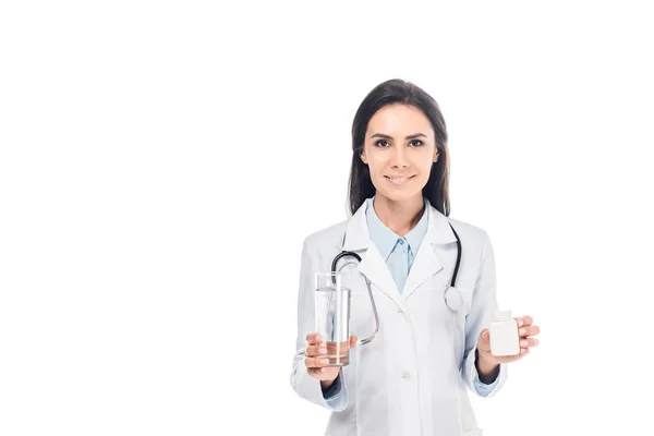 Улыбающийся доктор держит стакан воды и таблетки изолированы на белом — стоковое фото