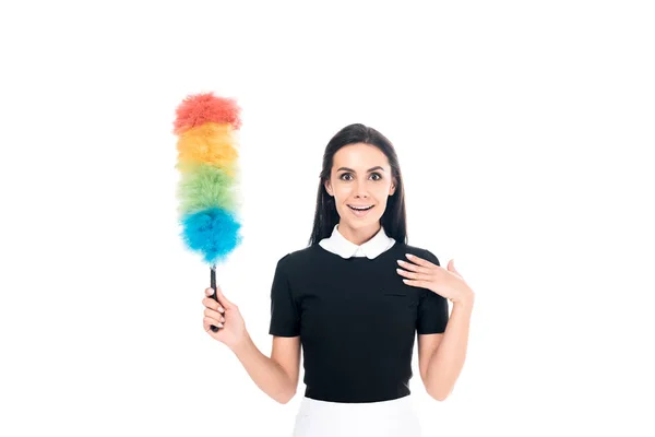 Surprised maid in uniform holding duster isolated on white — Stock Photo