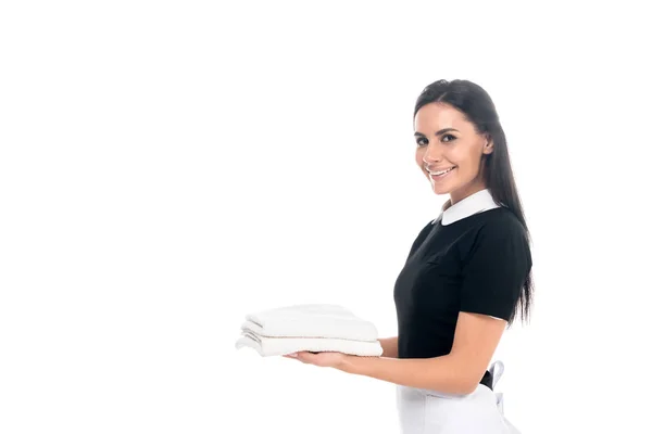 Smiling maid in uniform holding towels isolated on white — Stock Photo