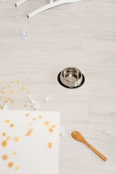 Selective focus of metal bowl, wooden spoon and broken dishes on floor in kitchen — Stock Photo