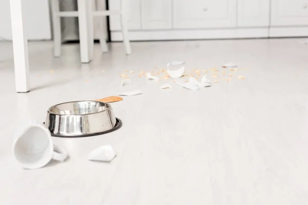 Selective focus of metal bowl and broken dishes on floor in messy kitchen — Stock Photo