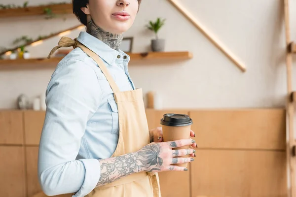 Partial view of tattooed waitress in apron holding disposal cup — Stock Photo