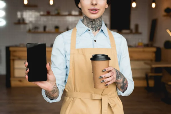 Vista parziale della cameriera in possesso di tazza di carta e smartphone con schermo bianco — Foto stock