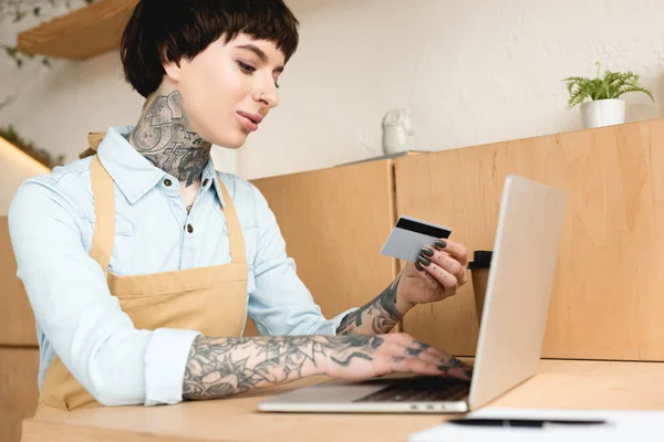 Atractiva camarera mirando la tarjeta de crédito y la escritura en el cuaderno - foto de stock