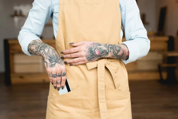 Visão parcial da garçonete tatuada colocando cartão de crédito no bolso do avental — Fotografia de Stock