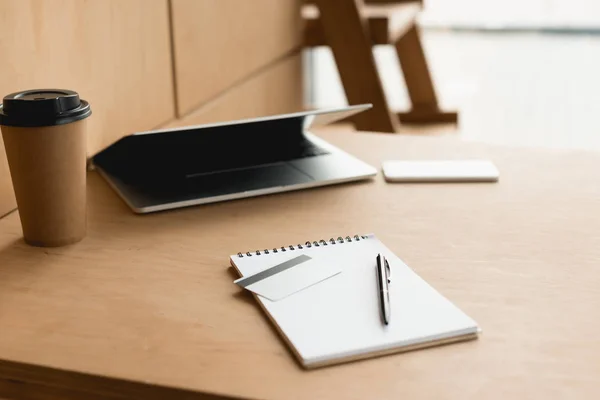 Enfoque selectivo de la mesa woode con ordenador portátil, taza de papel, portátil y tarjeta de crédito en la cafetería - foto de stock