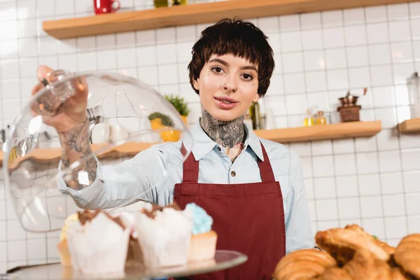 Foco seletivo de belo barista em pé perto de deliciosas sobremesas e olhando para a câmera — Fotografia de Stock