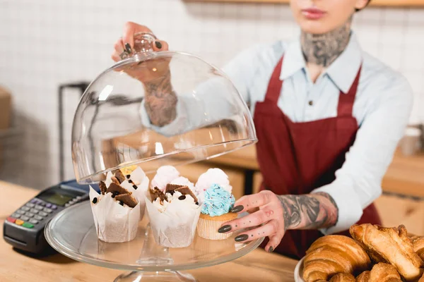 Partial view of barista in apron near bar counter with delicious desserts and payment terminal — Stock Photo
