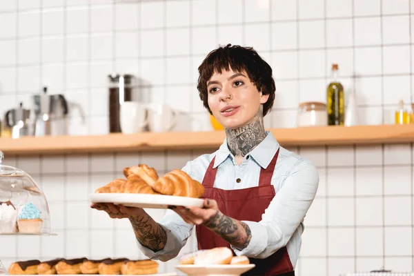 Smiling barista holding dish with croissants in outstretched hands — Stock Photo