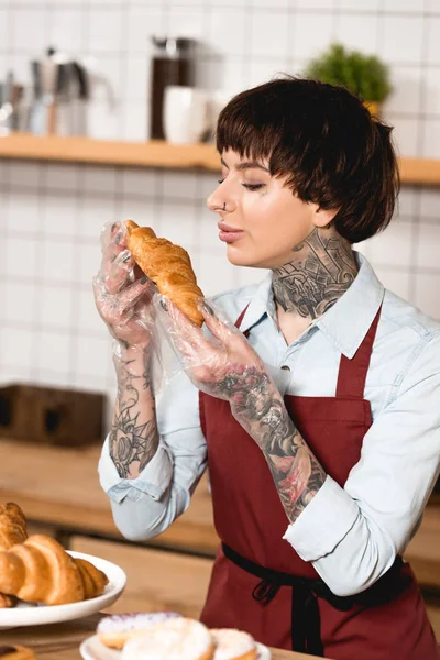 Pretty barista in disposable gloves holding delicious croissant — Stock Photo