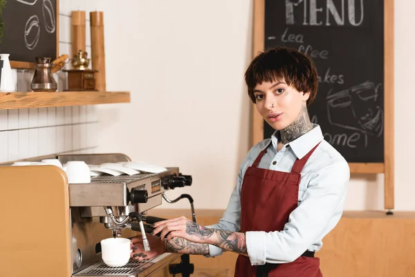 Muito tatuado barista preparar café na máquina de café e olhando para a câmera — Fotografia de Stock