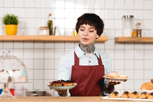 Atraente barista segurando pratos com deliciosa pastelaria no café — Fotografia de Stock