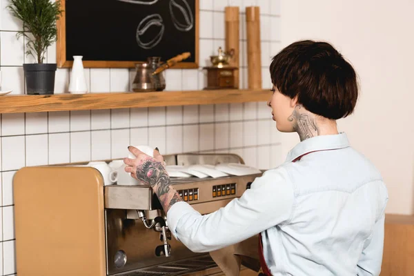Attractive tattooed barista standing near espresso machine in cafe — Stock Photo