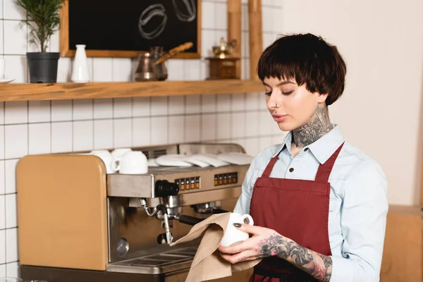 Schöne Barista Wischtasse, während sie in der Nähe der Espressomaschine im Café steht — Stockfoto