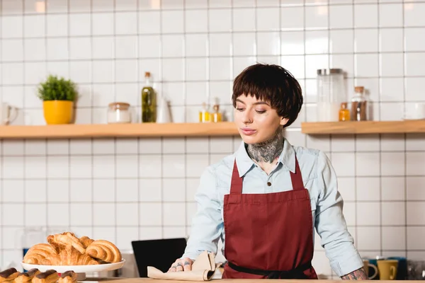 Attractive, tattooed barista in apron wiping bar counter with rag — Stock Photo