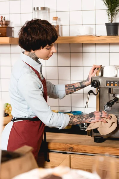 Selective focus of pretty barista cleaning espresso machine with rag in coffee shop — Stock Photo