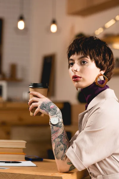 Beautiful businesswoman sitting with paper cup in coffee shop and looking away — Stock Photo