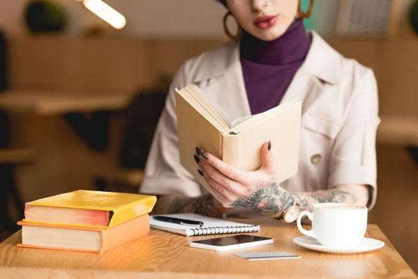 Частичный взгляд на деловую женщину, держащую книгу, сидя за столом в кафе — стоковое фото