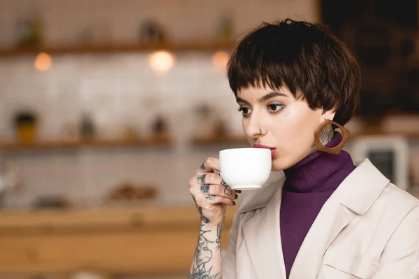 Nachdenkliche, modische Geschäftsfrau trinkt Kaffee aus weißer Kaffeetasse — Stockfoto