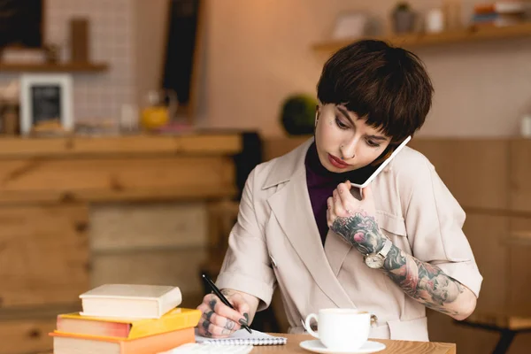 Bonita, mulher de negócios concentrada falando no smartphone enquanto sentado na cafetaria — Fotografia de Stock