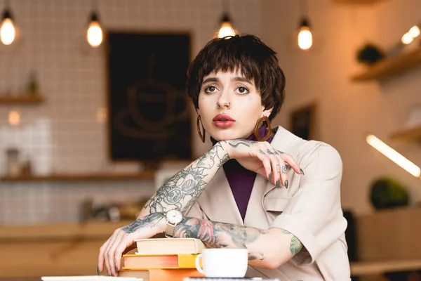 Pensativa empresaria sentada a la mesa con libros y taza de café en la cafetería - foto de stock