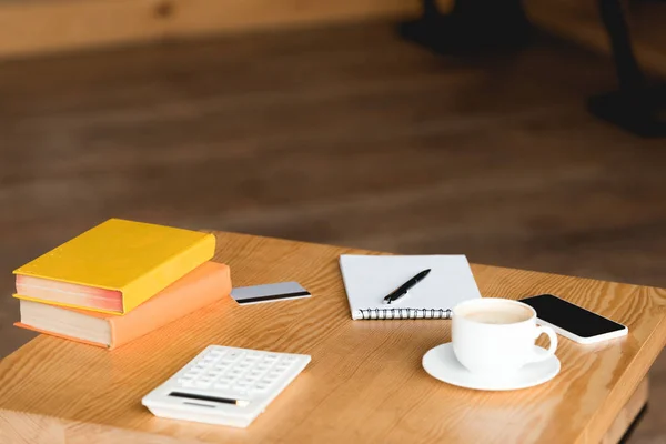 Table en bois avec livres, calculatrice, carte de crédit, tasse à café, ordinateur portable et smartphone avec écran blanc — Photo de stock