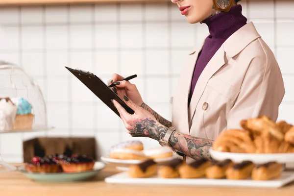 Partial view of businesswoman writing in clipboard in cafeteria — Stock Photo